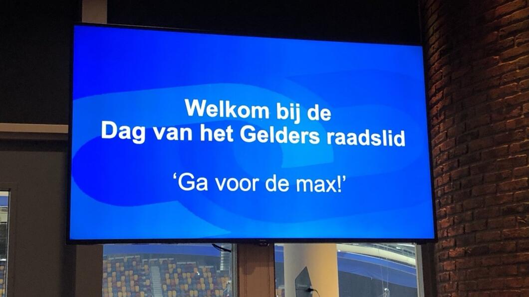 Beeldscherm met daarop het motto: "Ga voor de max!"